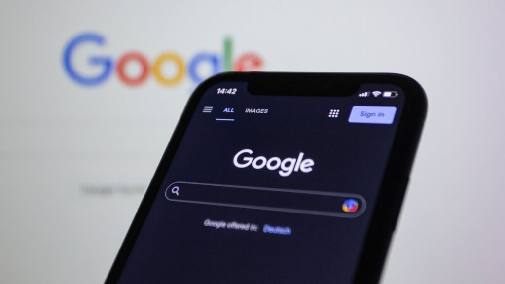 Photo by Bastian Riccardi Smartphone screen showing Google search in dark mode with the Google logo in the background.