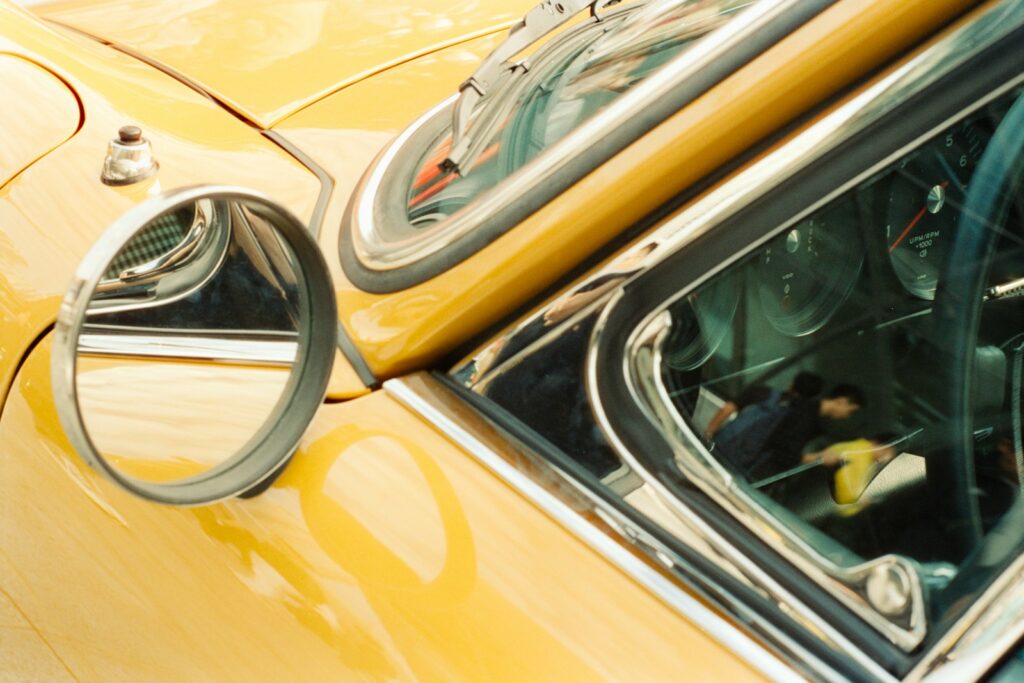 Close-up of a yellow vintage car's side mirror.